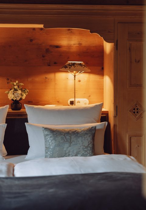 Hotelzimmer mit Doppelbett, Holzwand, zwei Lampen und Kissen in warmer Beleuchtung.