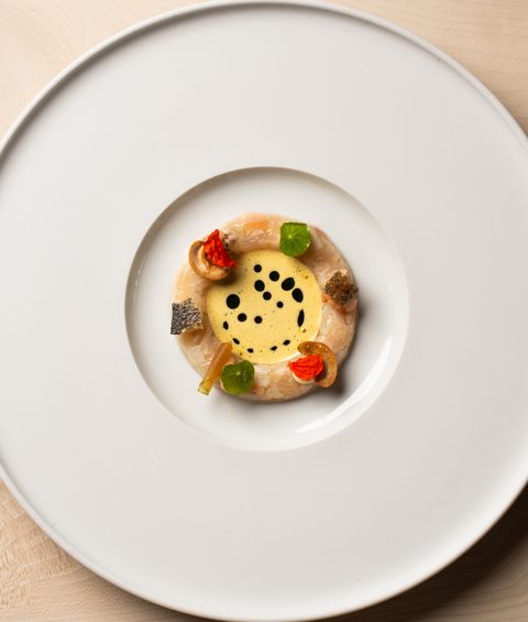 Artfully plated appetizer on a large white plate, viewed from above on a light wooden table.