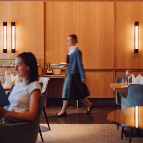 Ein Gast mit Speisekarte sitzt im Restaurant, während eine Servicekraft durch den Gastraum geht.