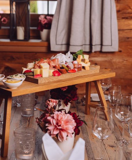 Gedeckter Restauranttisch mit Brotzeitplatte, kleinen Schalen und Blumendekoration in rustikalem Holzambiente.