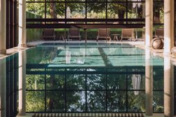 Innenpool mit großer Glasfront, Holzdecke und Liegen vor einem Garten.