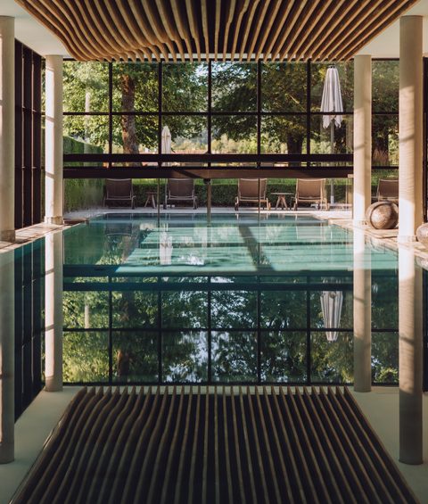 Innenpool mit großer Glasfront, Holzdecke und Liegen vor einem Garten.