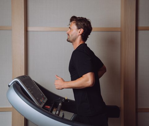 Ein Mann läuft auf einem Laufband in einem Fitnessraum mit Holzpaneelen.