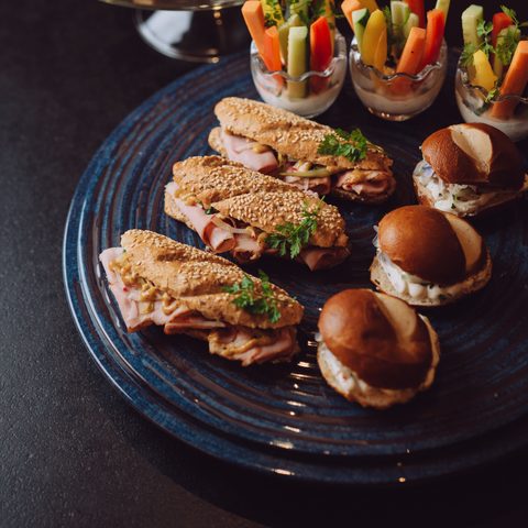 Buffet mit Sandwiches, Mini-Burgern, Gemüsesticks mit Dip und kleinen Desserts auf Tellern und Etagere.