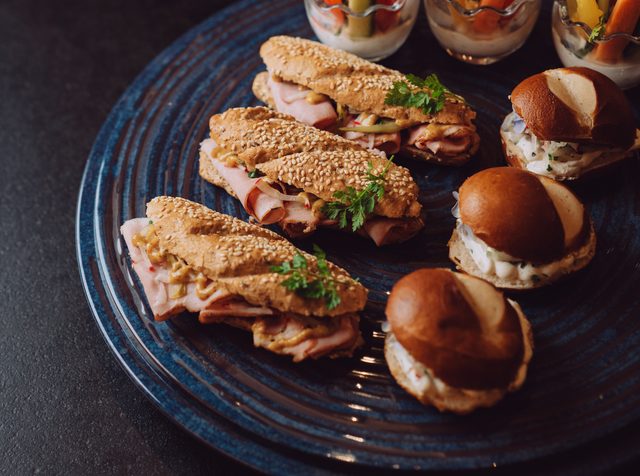 Buffet mit Sandwiches, Mini-Burgern, Gemüsesticks mit Dip und kleinen Desserts auf Tellern und Etagere.