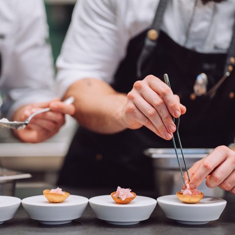 Two chefs garnish small appetizers on white bowls in a restaurant kitchen.