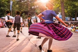 Kinder und Jugendliche tanzen in bayerischer Tracht auf einer Freiluftbühne vor Publikum im Wald.