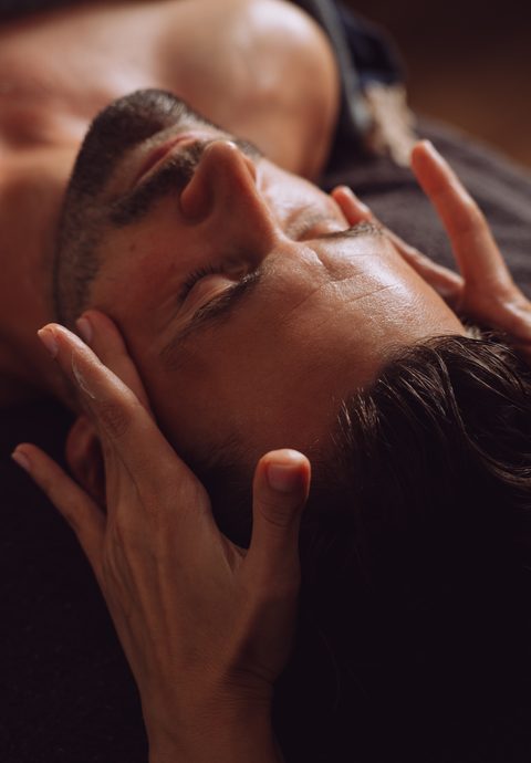 Ein Mann liegt bei einer Gesichts- und Kopfmassage im Wellnessbereich mit geschlossenen Augen.