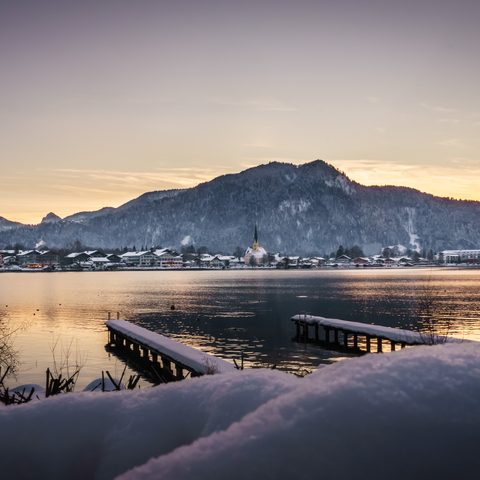 Snowy lake with two piers, village and mountains in the evening light.