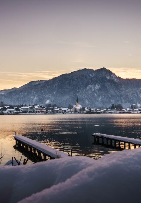Snowy lake with two piers, village and mountains in the evening light.