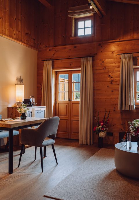 Wohnbereich im Chalet mit Holzwänden, Sofa, Sesseln, Tisch, Fenstern und Tür.