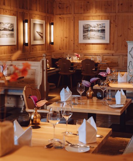 Restaurantstube mit Holzvertäfelung, gedeckten Tischen und Sitzbänken im warmen Innenraum.