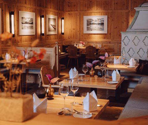 Restaurantstube mit Holzvertäfelung, gedeckten Tischen und Sitzbänken im warmen Innenraum.