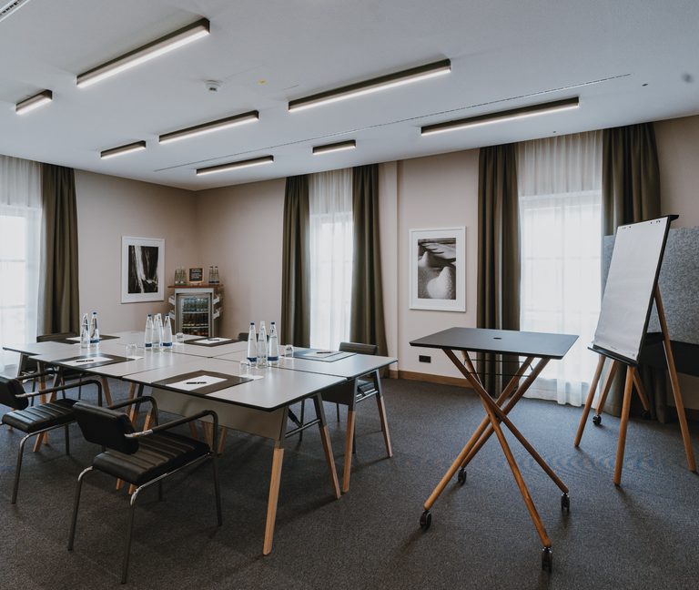 Seminarraum mit Tischen, Stühlen, Flipchart und Wasserflaschen für Besprechungen oder Workshops.