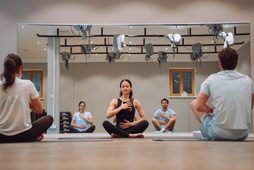 Kleine Gruppe bei einer Yoga- und Meditationseinheit im Fitnessraum vor einer Spiegelwand.