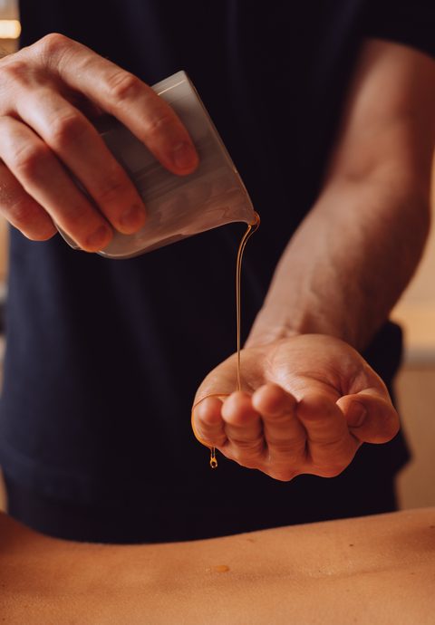 Ein Masseur gießt Öl in die Hand über dem Rücken einer Person auf einer Massageliege.