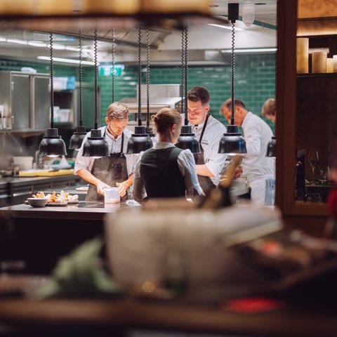 Köche und Servicepersonal arbeiten in einer offenen Restaurantküche am Pass.