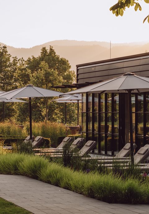 Outdoor spa area with loungers, parasols, a garden path and mountains in the background.
