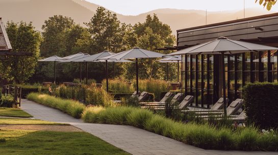 Outdoor spa area with loungers, parasols, a garden path and mountains in the background.
