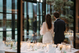 Bride and groom stand in a festively set restaurant with candles, flowers and glasses.