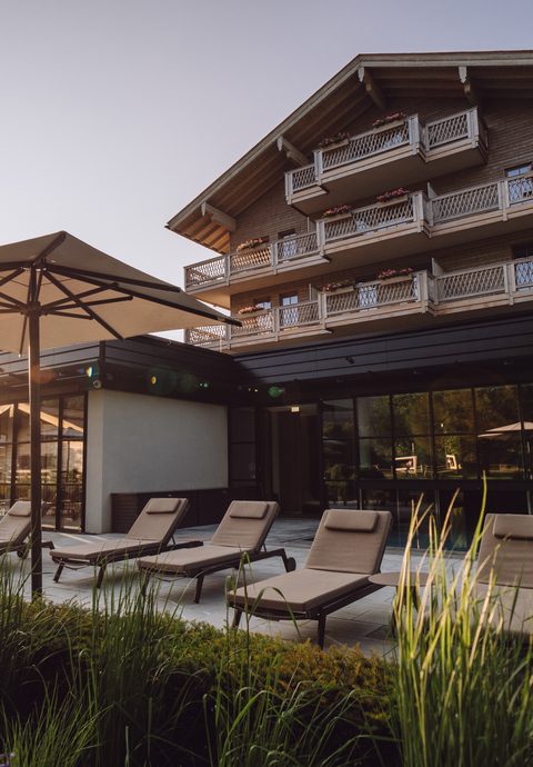 Liegestühle und Sonnenschirme auf der Hotelterrasse vor einem mehrstöckigen Gebäude im Abendlicht.