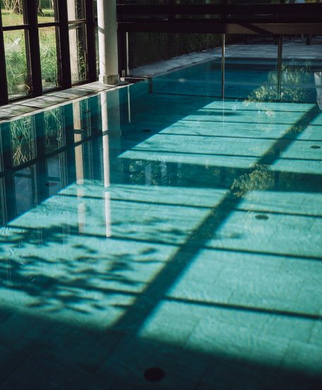 Innenpool mit großer Glasfront und Sonnenlicht auf der Wasseroberfläche.