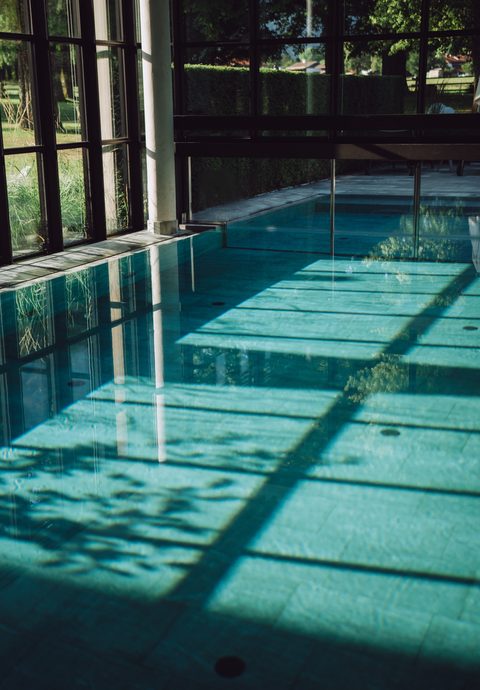 Indoor pool with large glass windows and sunlight on the water surface.