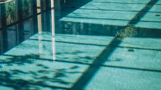 Indoor pool with large glass windows and sunlight on the water surface.