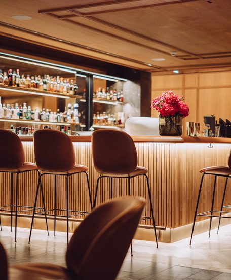 Warm beleuchtete Hotelbar mit Bartresen, Barhockern und Spirituosenregalen im Innenraum.