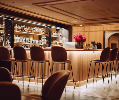 Warm beleuchtete Hotelbar mit Bartresen, Barhockern und Spirituosenregalen im Innenraum.