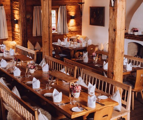 Rustikaler Restaurantbereich mit gedeckten Holztischen, Bänken und Kamin in einer holzverkleideten Stube.