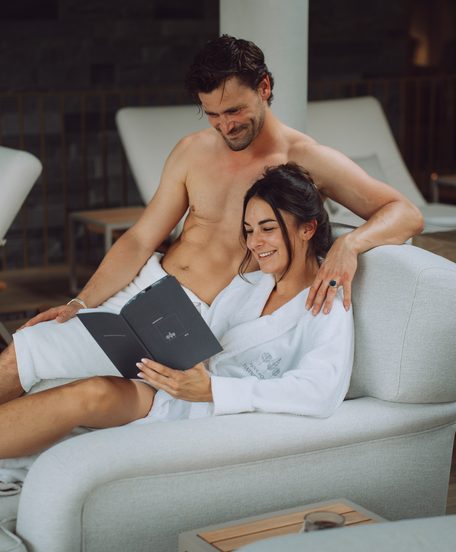 Ein Paar sitzt im Wellnessbereich auf einer Liege und liest gemeinsam eine Broschüre.