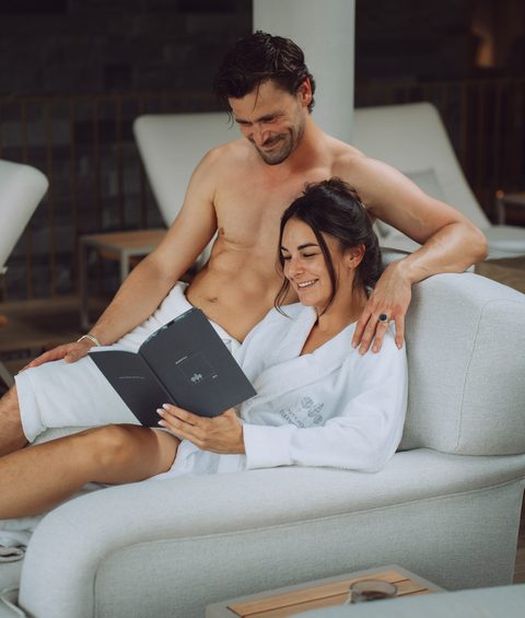 Ein Paar sitzt im Wellnessbereich auf einer Liege und liest gemeinsam eine Broschüre.