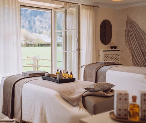 Wellness-Behandlungsraum mit zwei Liegen, Ölen und offenem Fenster mit Blick auf Wiese und Garten.