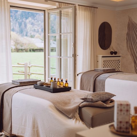 Wellness treatment room with two beds, oils and open window overlooking meadow and garden.