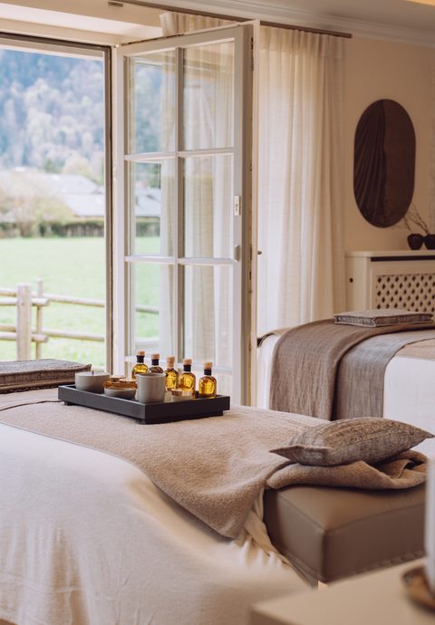 Wellness-Behandlungsraum mit zwei Liegen, Ölen und offenem Fenster mit Blick auf Wiese und Garten.