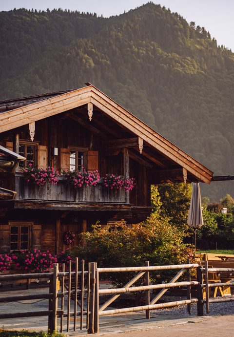 Traditionelles Holzchalet mit Blumen am Balkon vor einem bewaldeten Berghang.