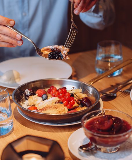 Dessert mit frischen Beeren auf einem Restauranttisch, dazu Weißwein, Wasser und gedecktes Geschirr.