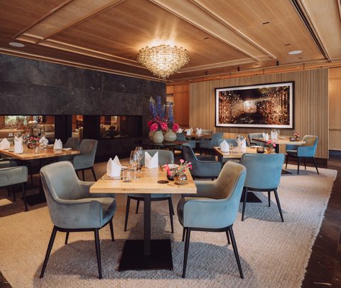 Restaurantinnenraum mit gedeckten Tischen, Sesseln, Kaminwand und Kronleuchter.