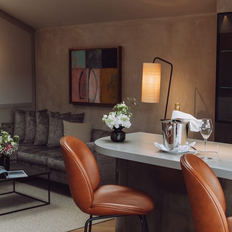 Suite living area with sofa, counter, two bar stools, flowers, and a wine cooler on the surface.