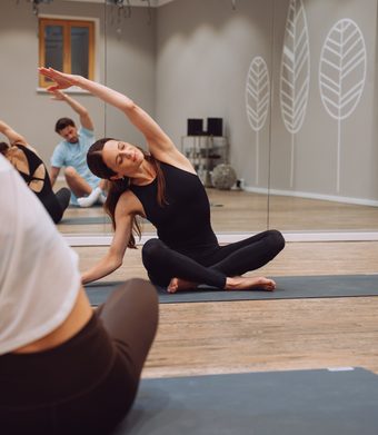 Mehrere Personen machen Yoga auf Matten in einem Fitnessraum mit Spiegelwand.