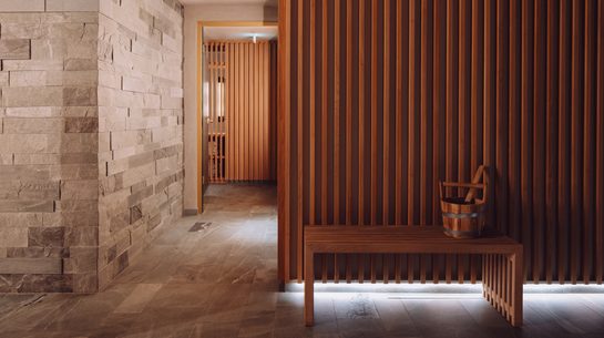 Wellness corridor with wooden slat wall, bench, and bucket in front of the sauna area.