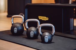 Drei Kettlebells auf einer Trainingsmatte vor Fitnessgeräten in einem Innenraum mit Holzverkleidung.