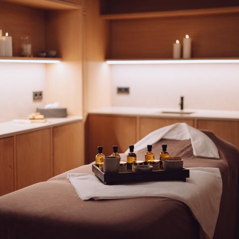 Wellness treatment room with massage table, oils on a tray, and candles in warm light.