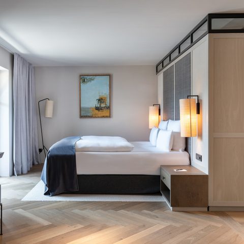 Modernes Hotelzimmer mit Doppelbett, Schreibtisch, Fernseher und offenem Badezimmerbereich.
