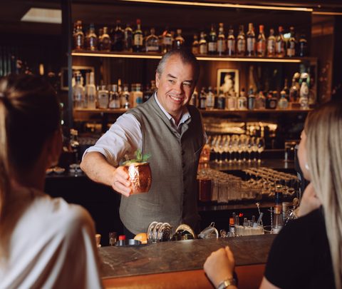Ein Barkeeper serviert zwei Gästen einen Cocktail an einer Hotelbar.
