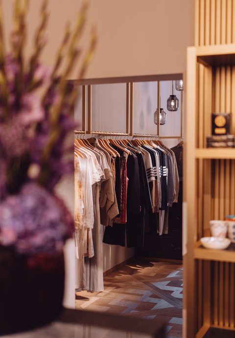 Boutique-Innenraum mit Kleiderständer, Kleidung, Spiegel und Holzregal.