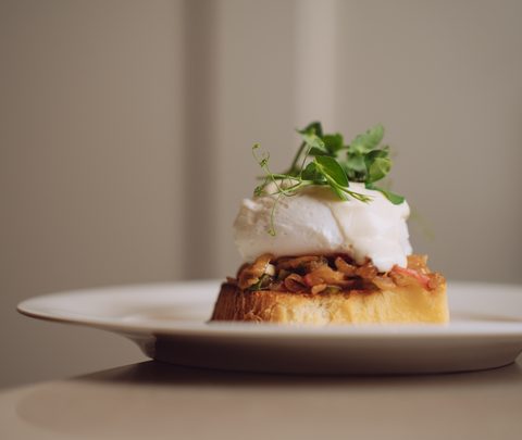 Toast mit pochiertem Ei, Pilzen und Kräutern auf einem weißen Teller.