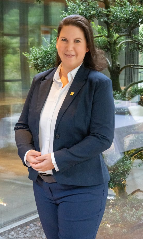Porträt einer Hotelmitarbeiterin im Business-Outfit in einem Innenbereich mit Pflanzen im Hintergrund.