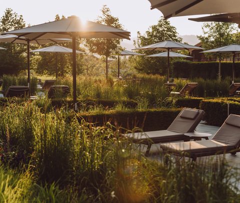 Sun loungers and parasols on a wellness terrace in a garden with low evening sunlight.